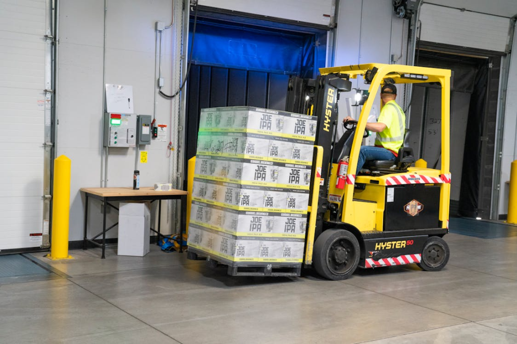 A man riding a yellow forklift with boxes in a distribution center