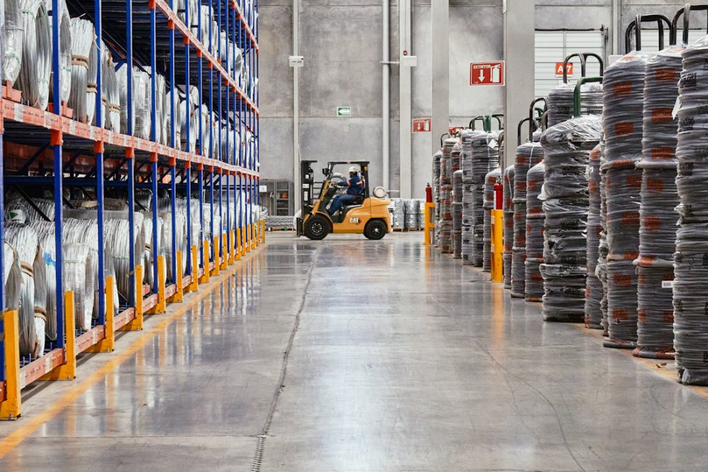 A man operating a forklift across the floors of an industrial warehouse.
