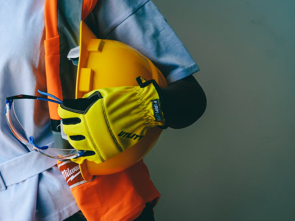 A close-up shot of a person wearing yellow safety gloves and holding a hard hat.
