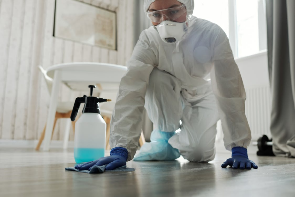 A woman in white overalls wiping the surface of a patient’s room.
